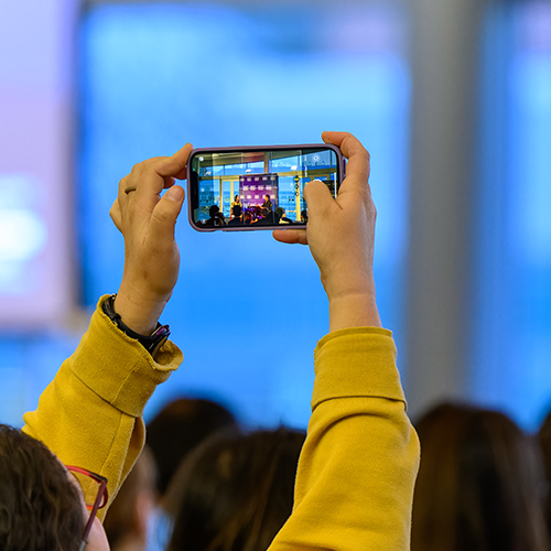 Someone taking a picture on their phone of a speaker on stage